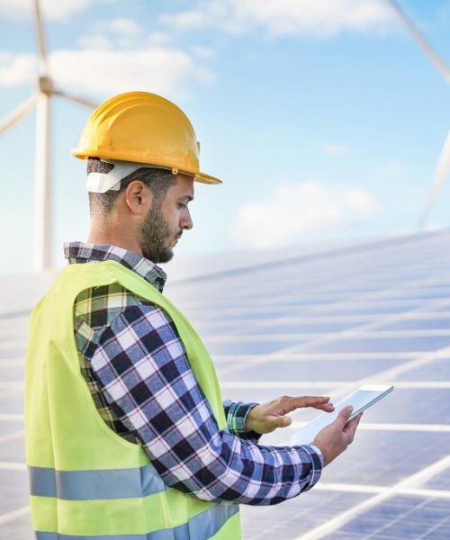 Man working at solar power station with digital tablet - Renewable energry with wind turbines and solar panels